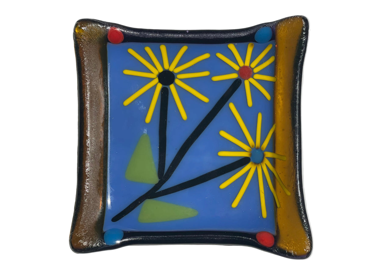 A square handmade fused glass dish with a blue center featuring yellow sunflower designs and a brown textured border.