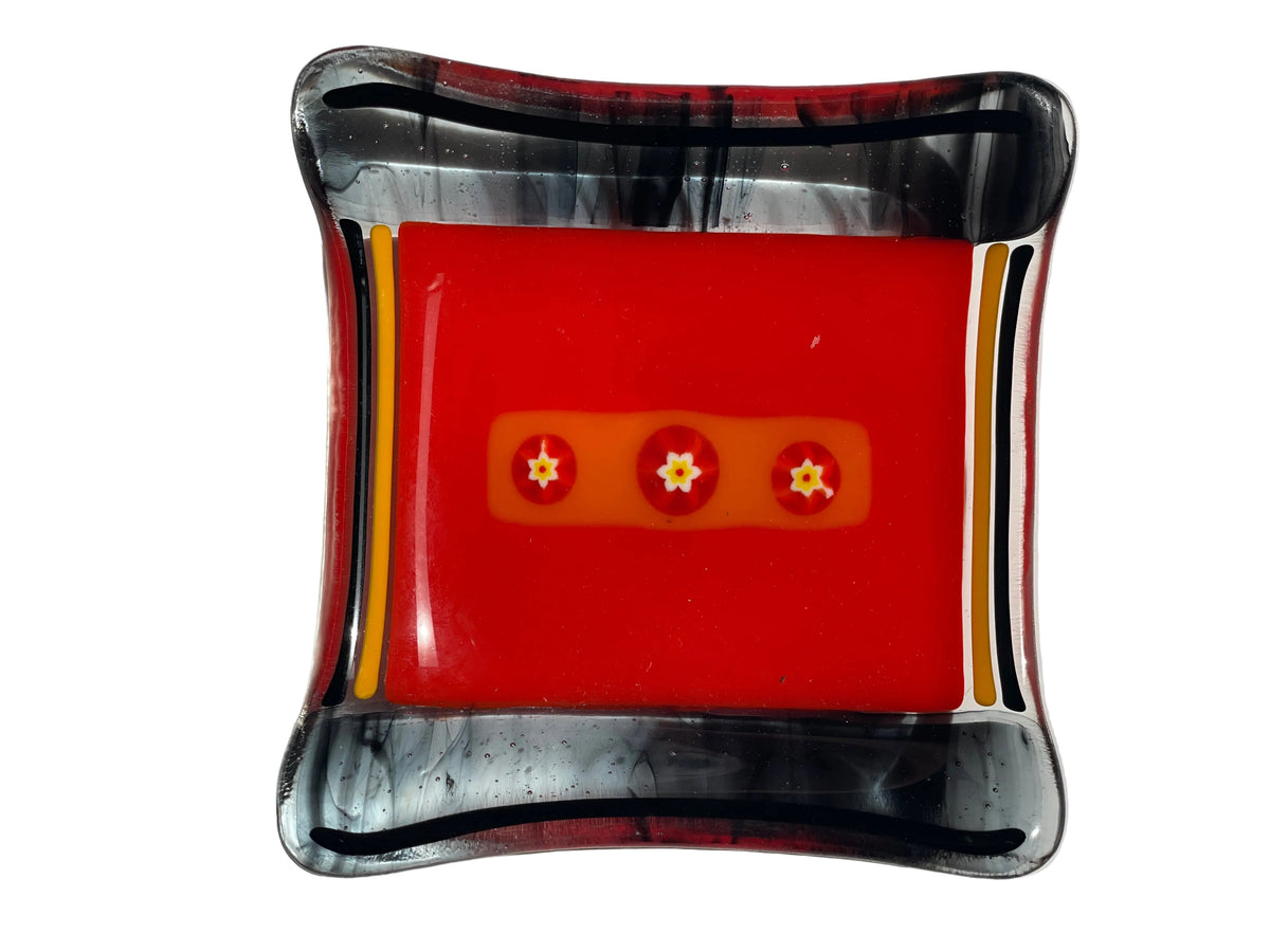 A square glass tray with rounded corners, featuring a vibrant red center, a yellow-orange band, and a marbled black and clear outer border.