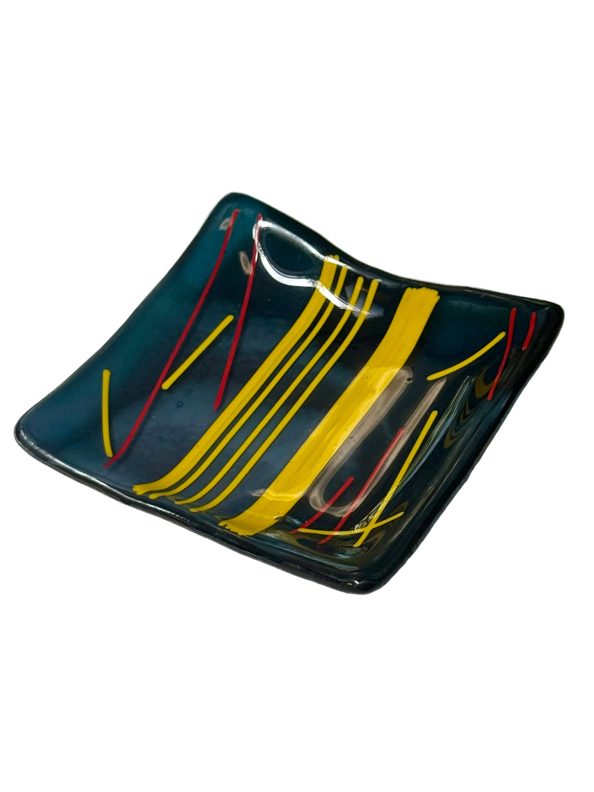 A square, shallow fused glass dish with a dark teal-blue base, decorated with bold yellow and thin red abstract lines.